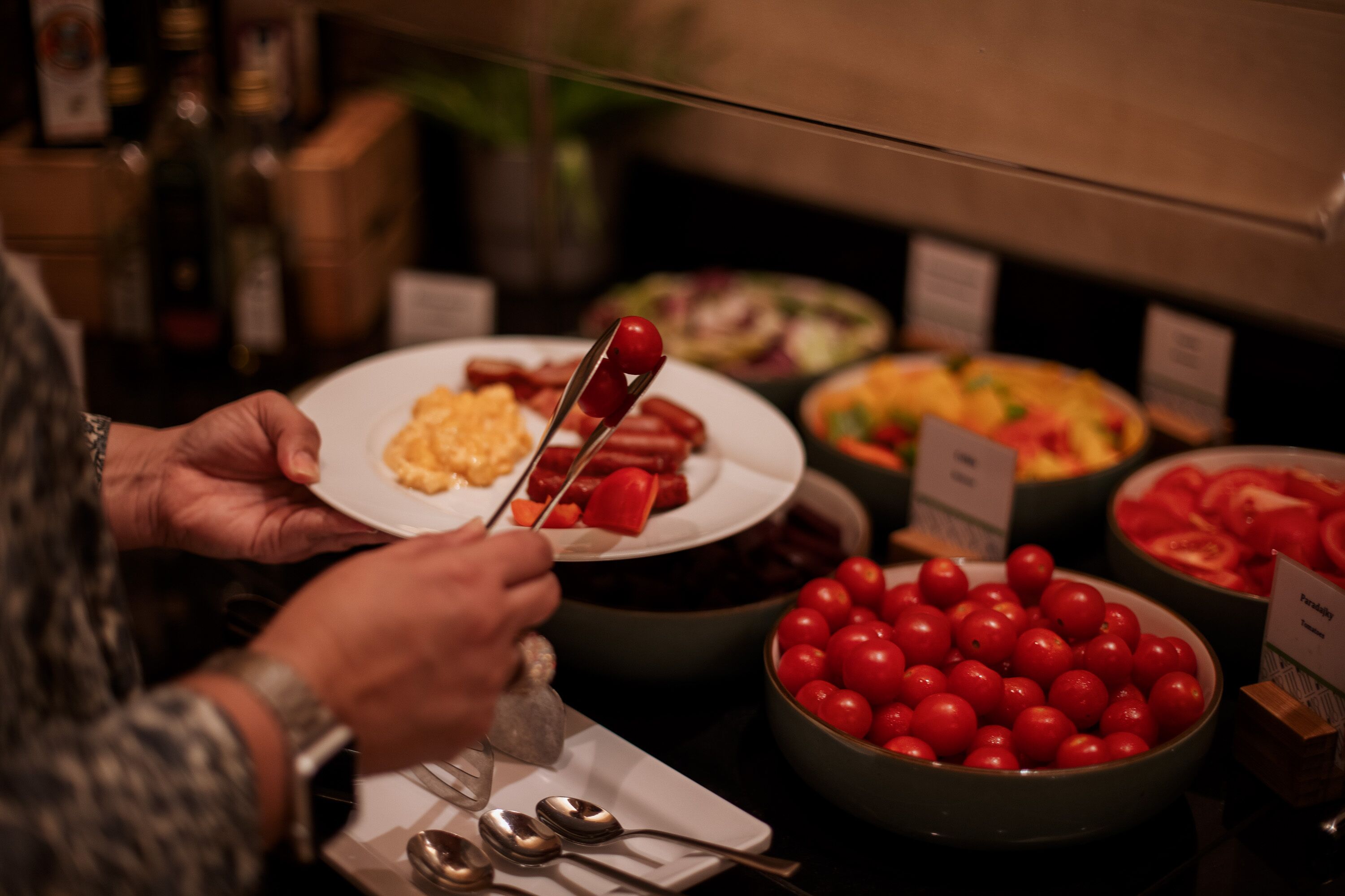 A buffet with various food items including a plate with cherry tomatoes, a bowl of sliced tomatoes, and a dish with scrambled eggs.