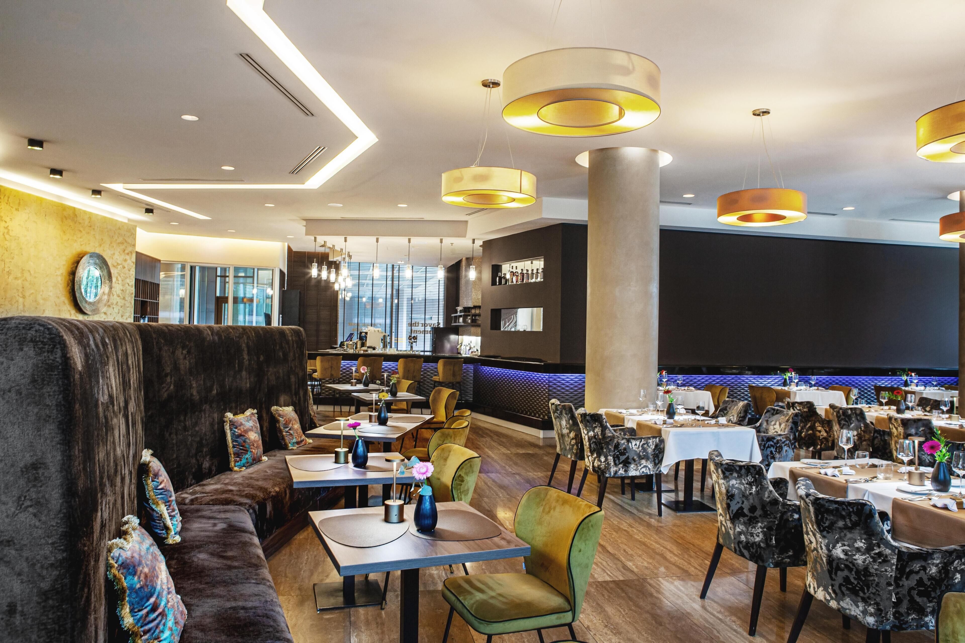 A modern restaurant with high tables, cushioned seating, and pendant lighting.