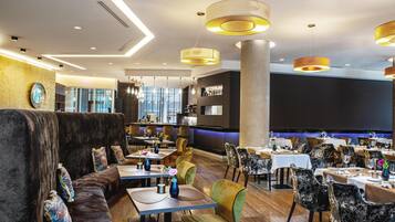 A modern restaurant with high tables, cushioned seating, and pendant lighting.