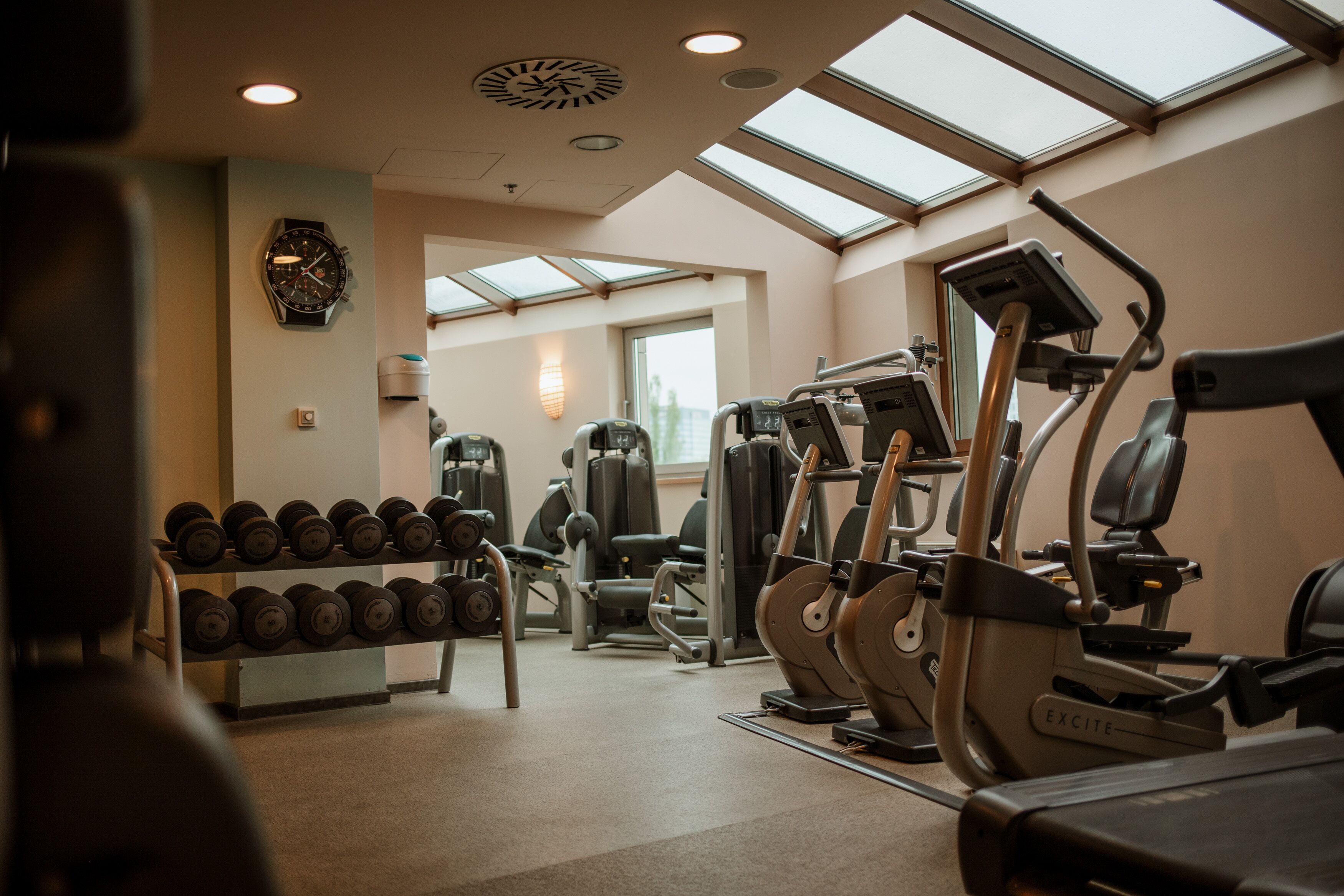 Une salle de sport équipée de matériel d’exercice, avec une horloge murale et un plafond vitré.