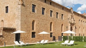 Un bâtiment en pierre doté d’une piscine, de chaises longues blanches et de parasols.