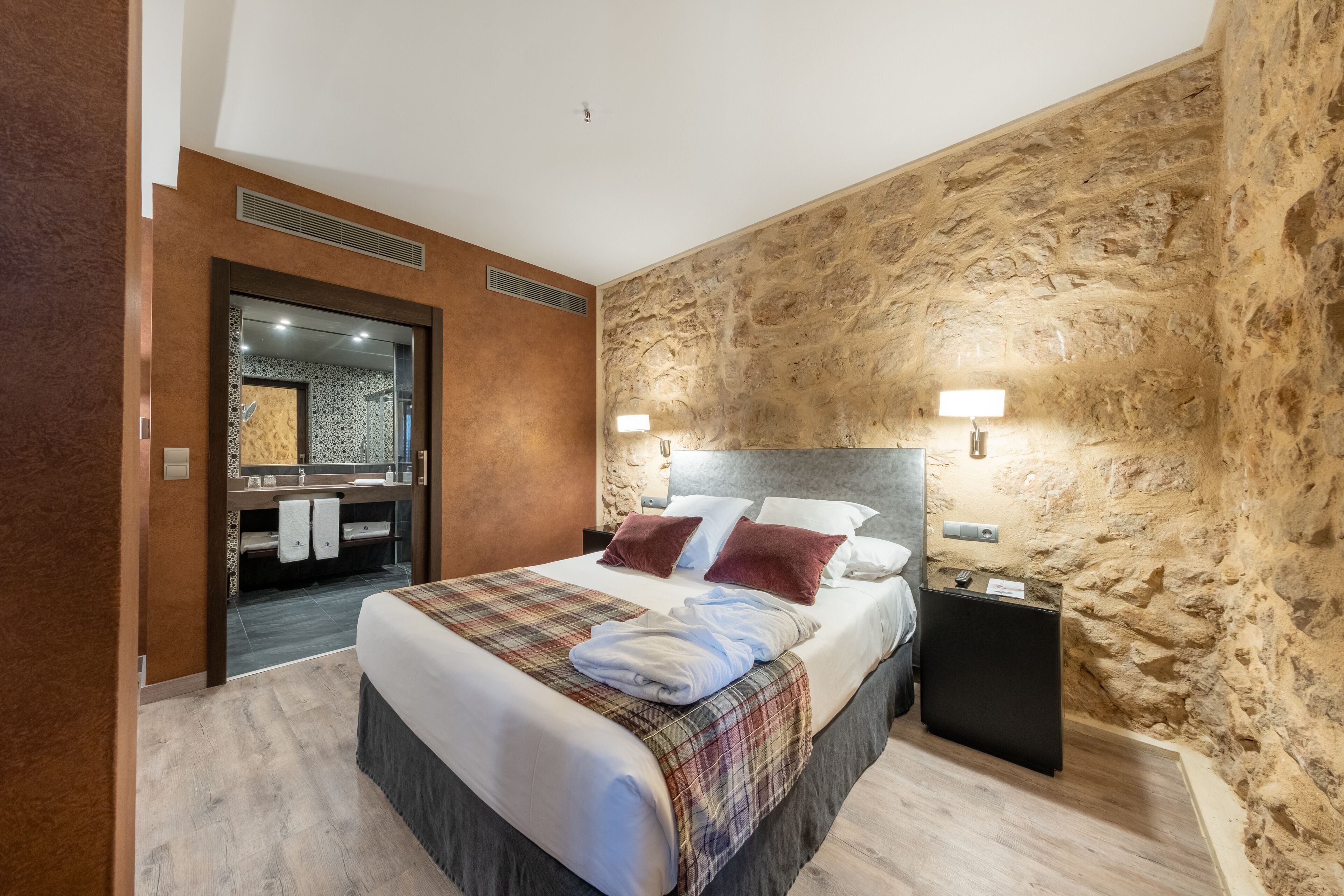 Una habitación de hotel moderna con una cama grande, un tocador integrado y una pared decorativa de piedra.