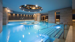 Une piscine intérieure moderne dotée d’un toit en verre, d’une eau cristalline et d’un espace détente avec des fauteuils.