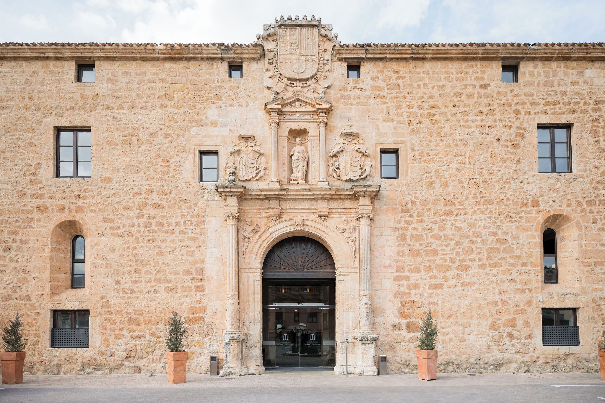 Um edifício de pedra com um arco central, janelas em arco e um brasão acima da entrada.