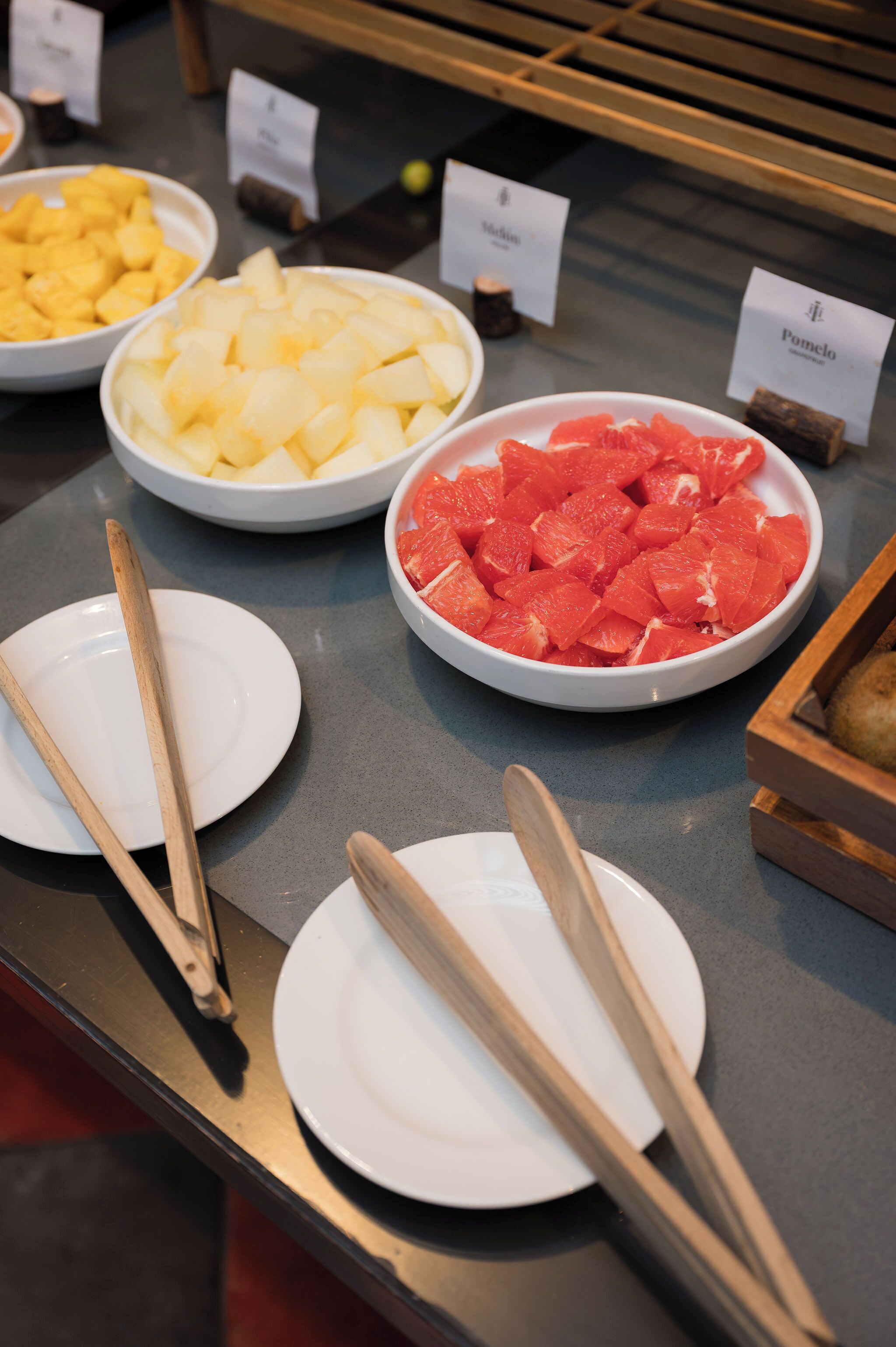A buffet with various fruits and a wooden cutting board.