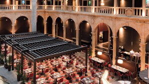 Un vaste espace intérieur à plusieurs niveaux, comprenant un espace central ouvert avec des tables et des chaises, entouré d’arcades et de colonnes.