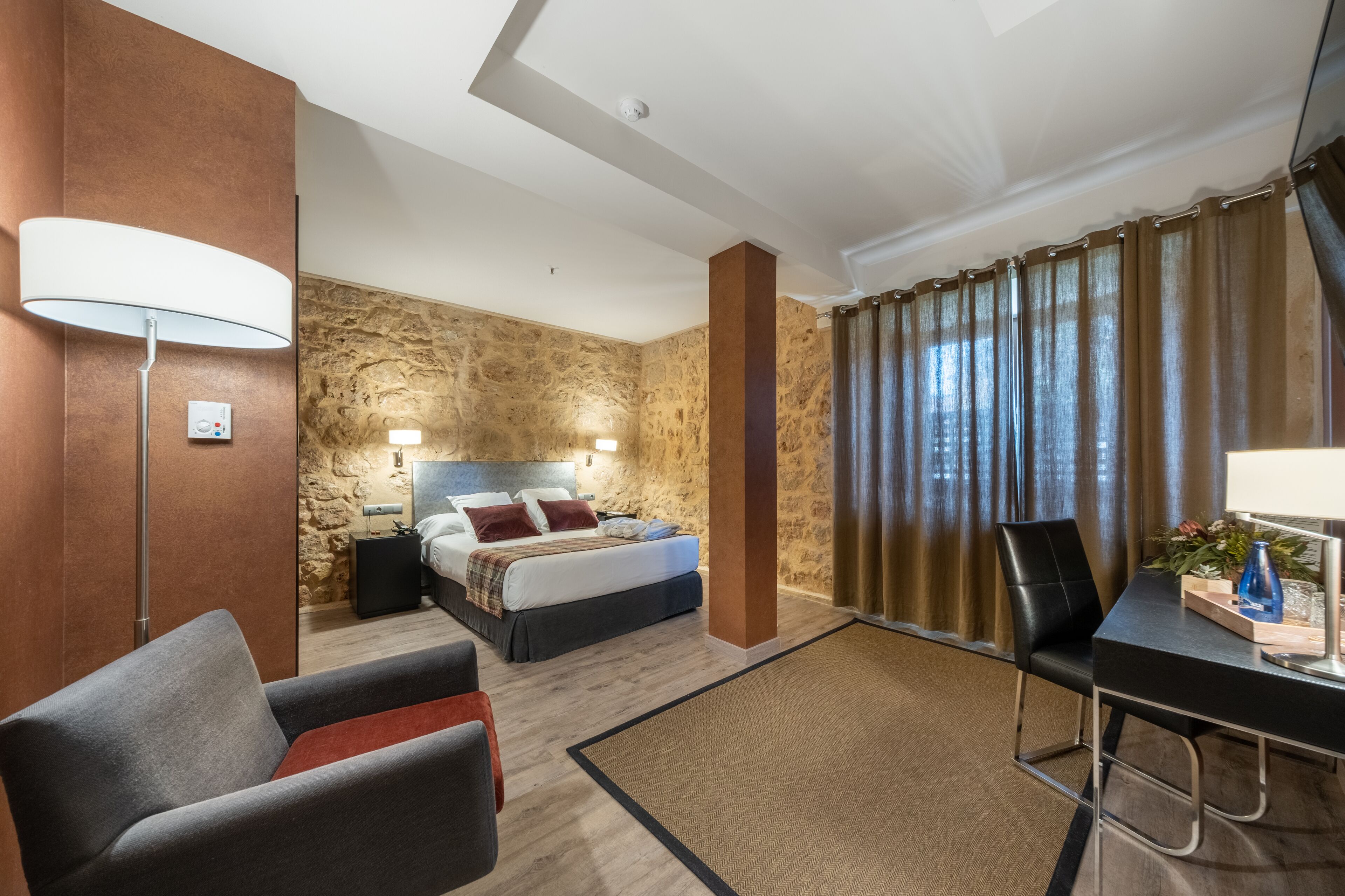 Een hotelkamer met een bed, bureau, stoel, lamp en nachtkastje.