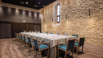 A conference room with a long table set for a meeting, wooden chairs, and a stone wall with a window.