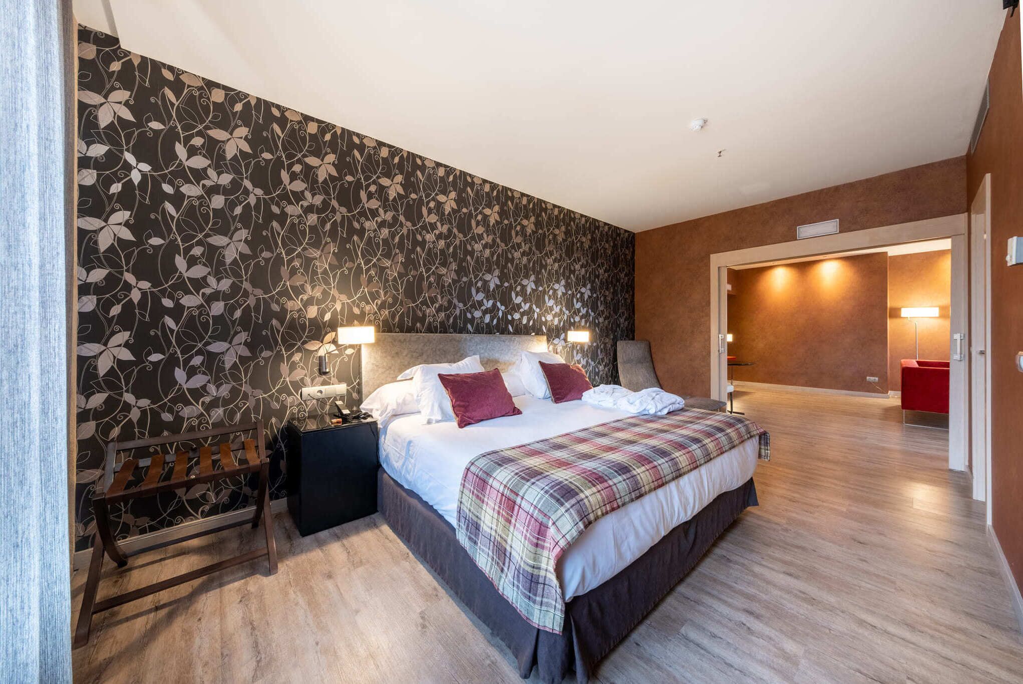 A bedroom with a bed, bedside tables, a bench, and a patterned wall.