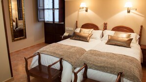 Habitación de hotel con una cama grande, dos mesitas de noche, un espejo y una ventana con cortinas.
