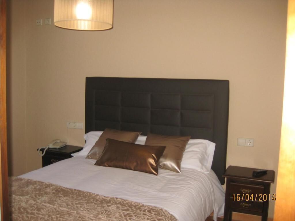 A hotel room with a large bed, a headboard, a bedside table, and a lamp.