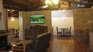 Un interior rústico con vigas de madera a la vista, una pared de piedra, un televisor montado y una chimenea.