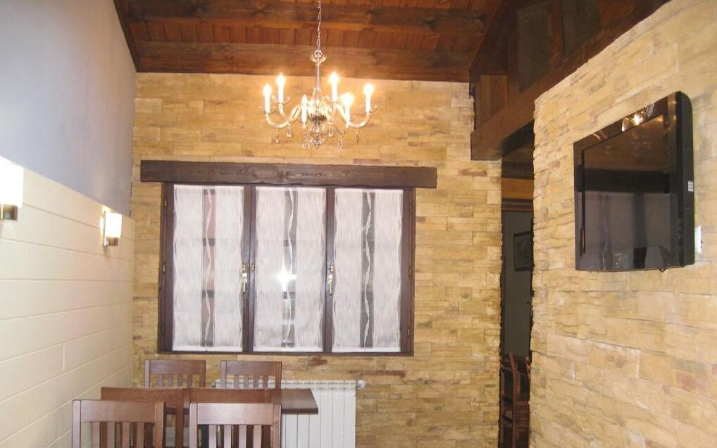 A dining area with a stone wall, a chandelier, and a window with curtains.