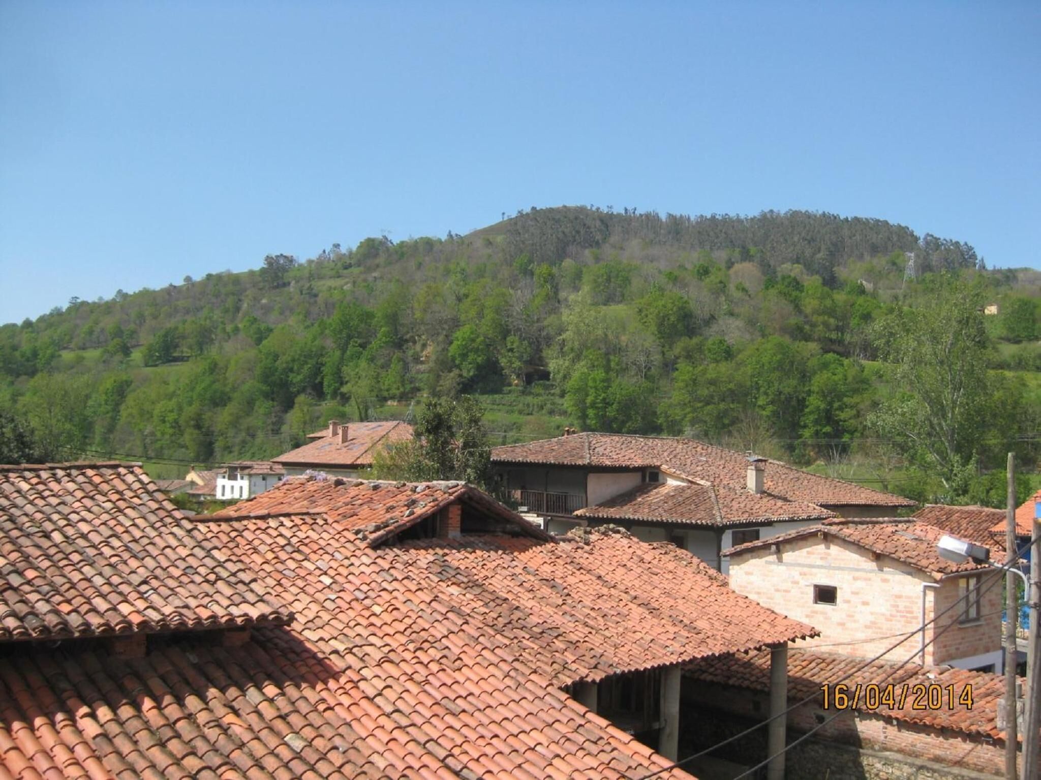 A rural village with traditional red-tiled roofs and buildings surrounded by lush green hills.
