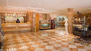 A lobby with a checkered floor, marble columns, a reception desk, and a statue.