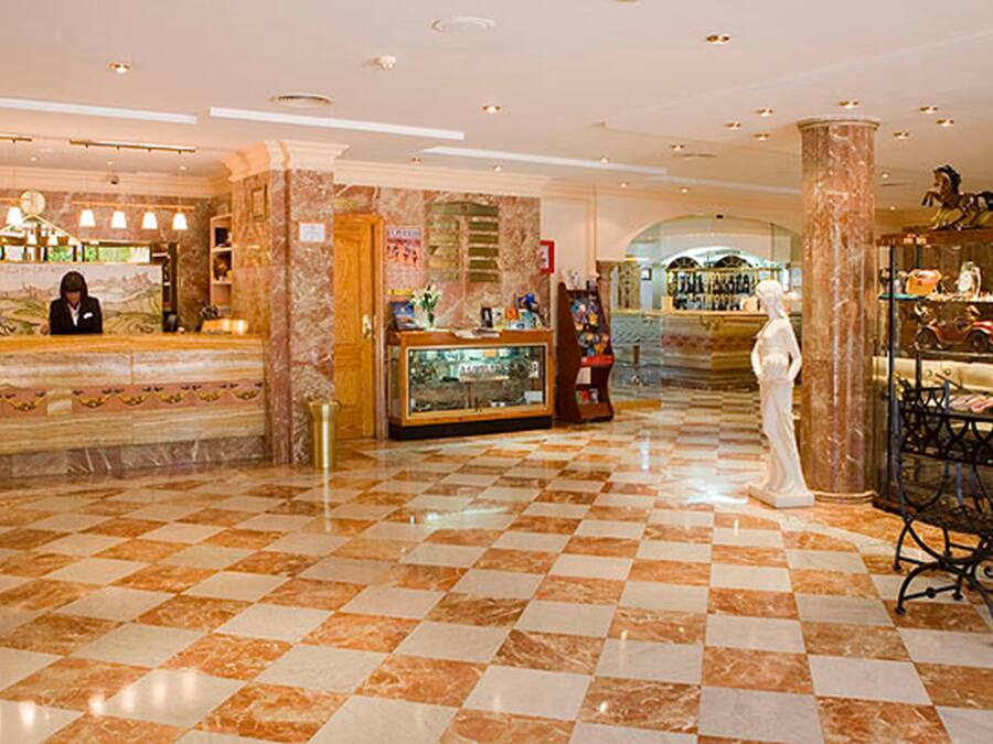 A lobby with a checkered floor, marble columns, a reception desk, and a statue.