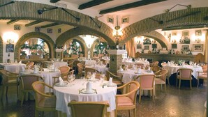 A restaurant with round tables, wooden chairs, and arched ceilings.