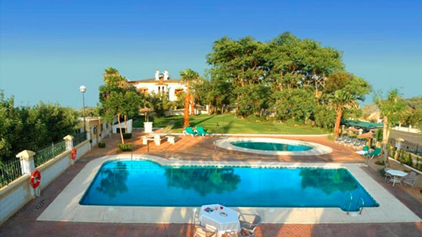 A rectangular swimming pool with a surrounding deck, a lawn, and a building in the background.