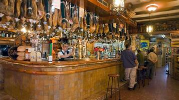 A bar with a tiled counter, hanging meats, and a vintage decor.