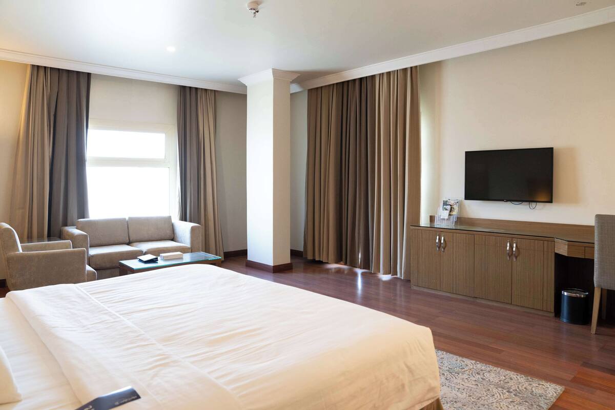 A hotel room with a large bed, a sofa, a TV, and a desk.