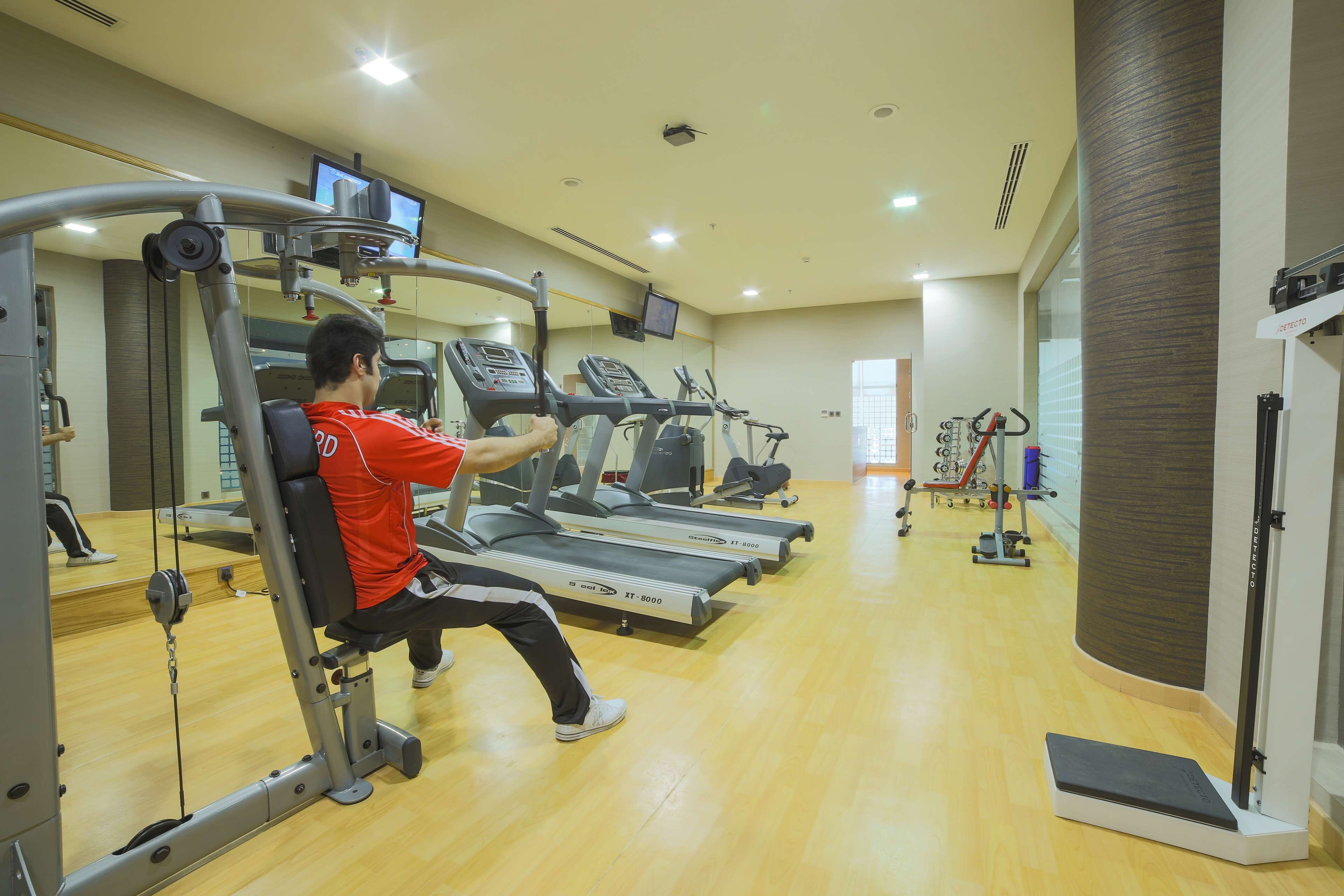 Un gimnasio con cintas de correr, máquinas de pesas y un espejo.
