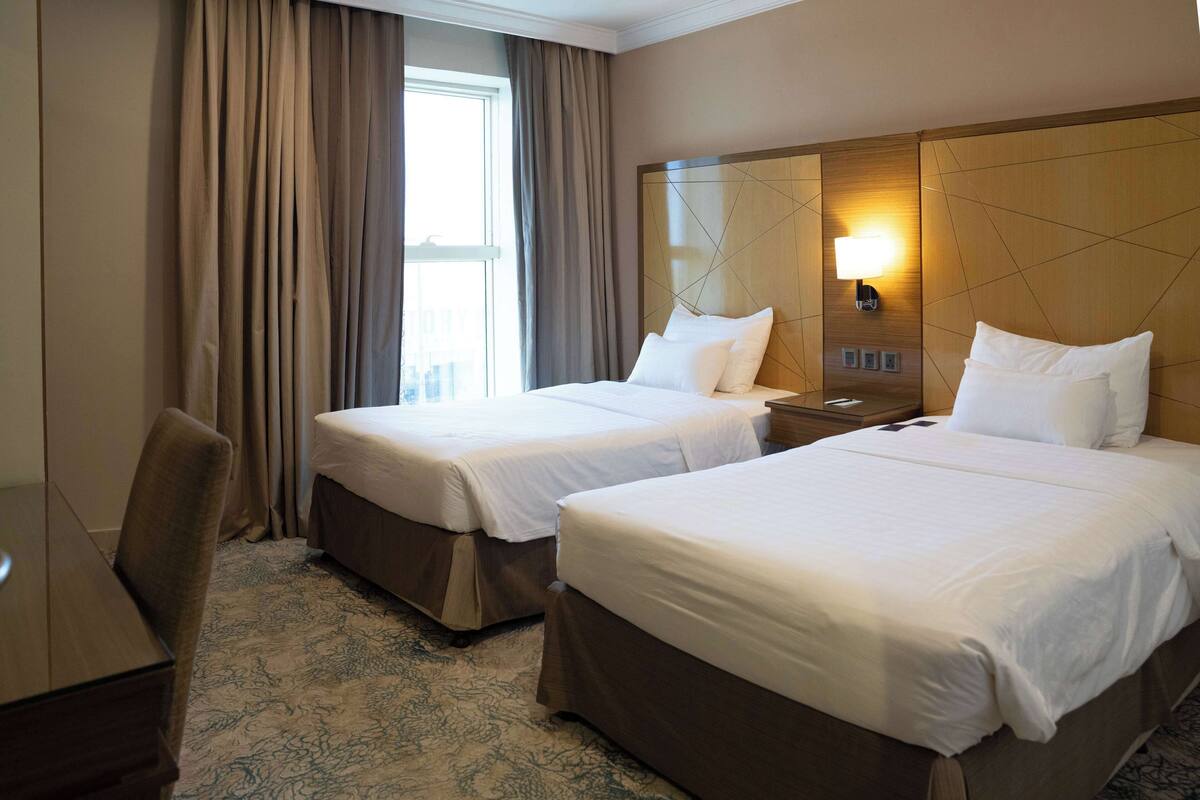A hotel room with two beds, a desk, and a large mirror.