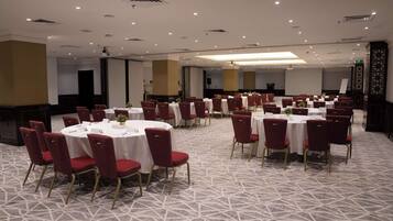 Un salón de conferencias con mesas redondas y sillas rojas, suelo alfombrado e iluminación empotrada.