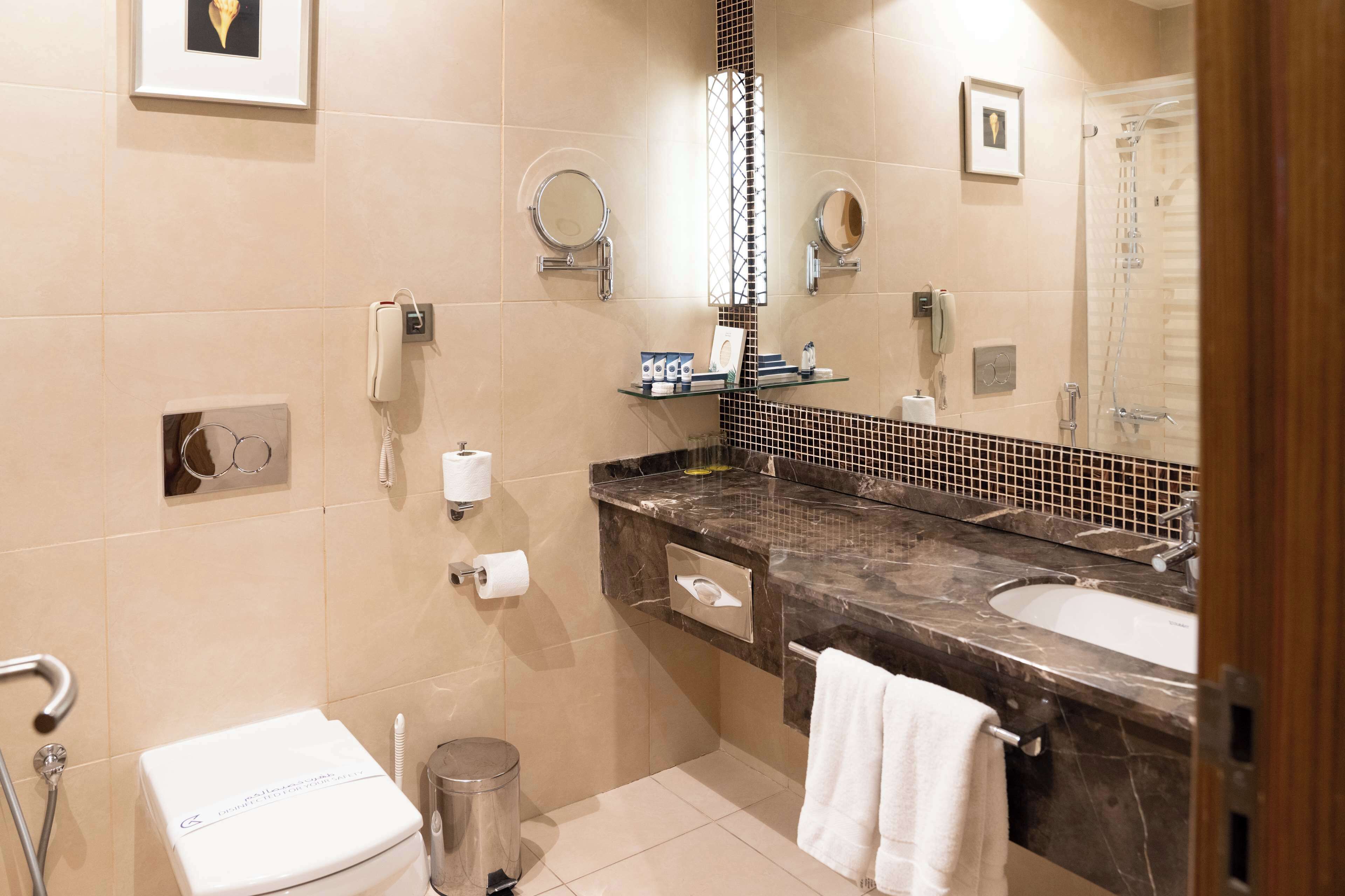 A modern bathroom with a marble sink, a toilet, a shower, and a mirror.