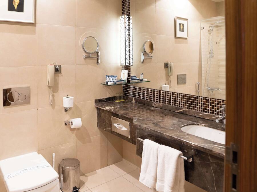 A modern bathroom with a marble sink, a toilet, a shower, and a mirror.