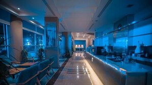 Un hall d’hôtel moderne avec un long comptoir d’accueil, un espace salon et de grandes fenêtres donnant sur la ville.