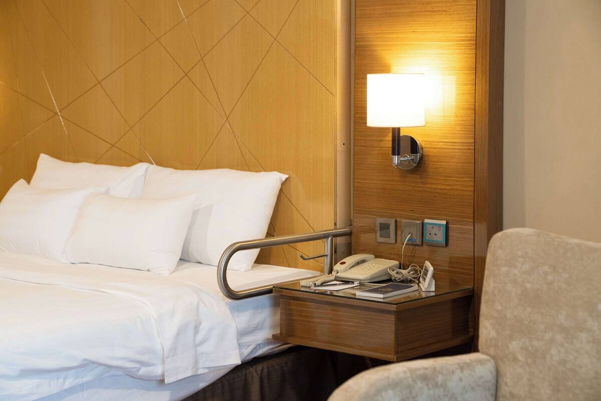 A hotel room with a bed, bedside table, lamp, and a chair.