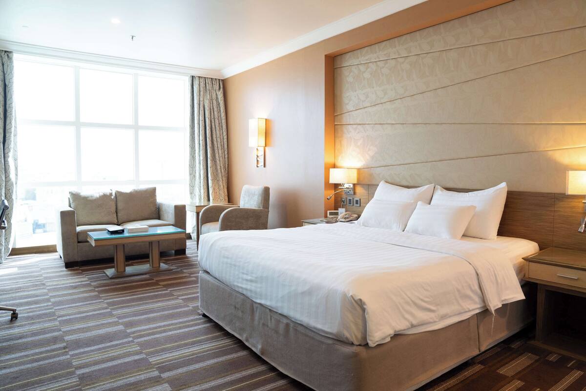 A hotel room with a large bed, a sofa, a small table, and a nightstand.