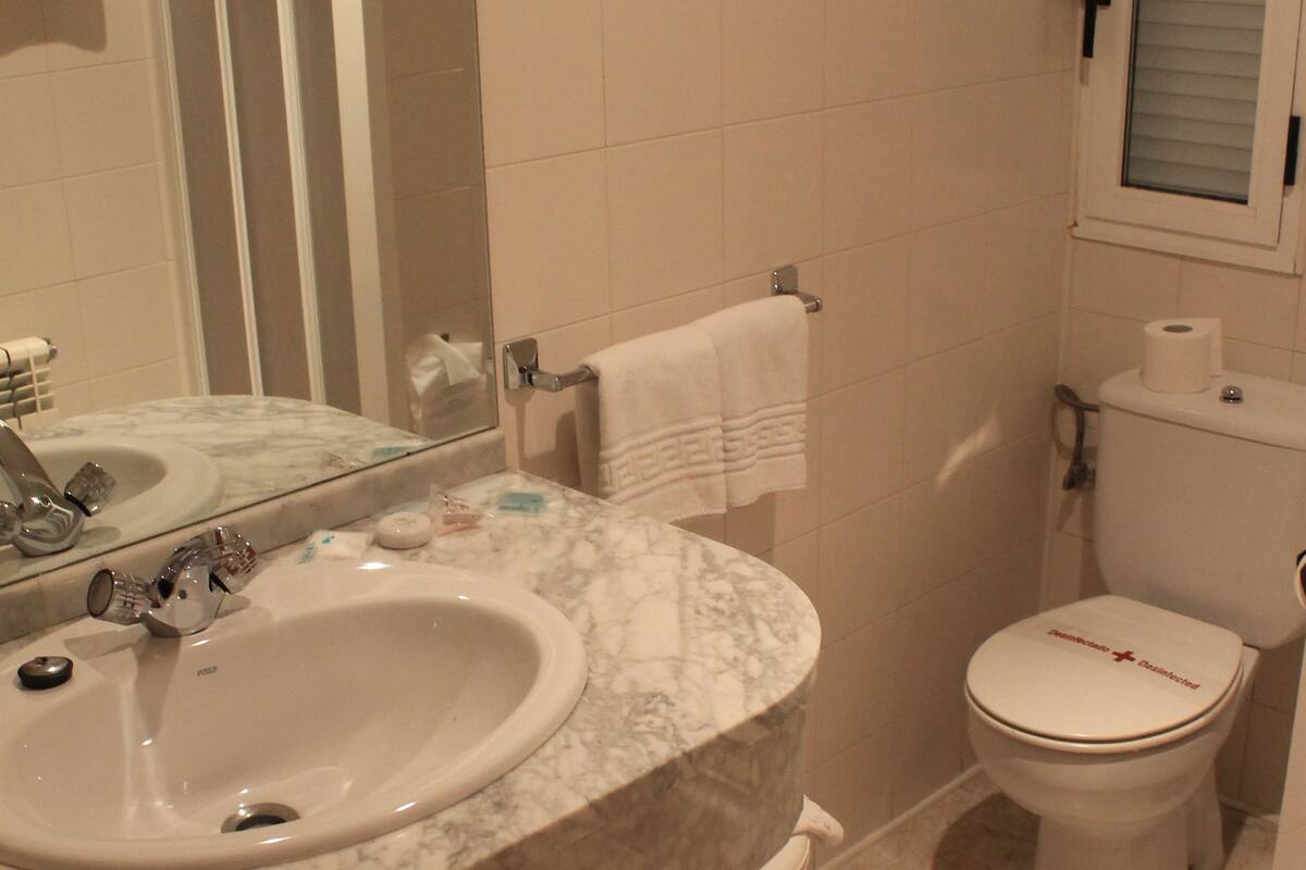 Un baño con lavamanos de mármol, inodoro y espejo.