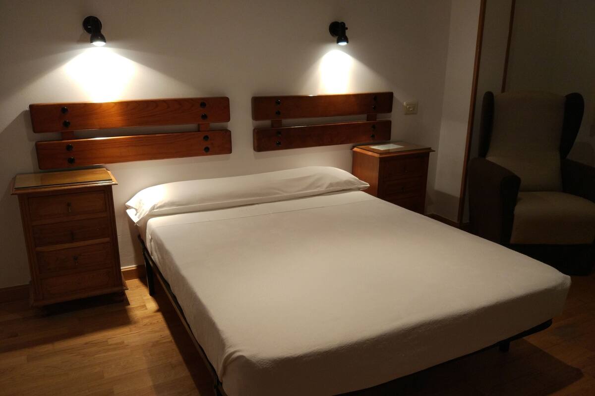 Una cama bien hecha con cabecera de madera, una mesita de noche y una silla.