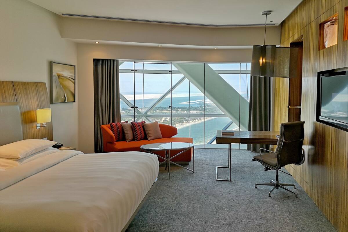 Ein Hotelzimmer mit Bett, Sofa, Schreibtisch, Stuhl, Fernseher und einem großen Fenster mit Blick.