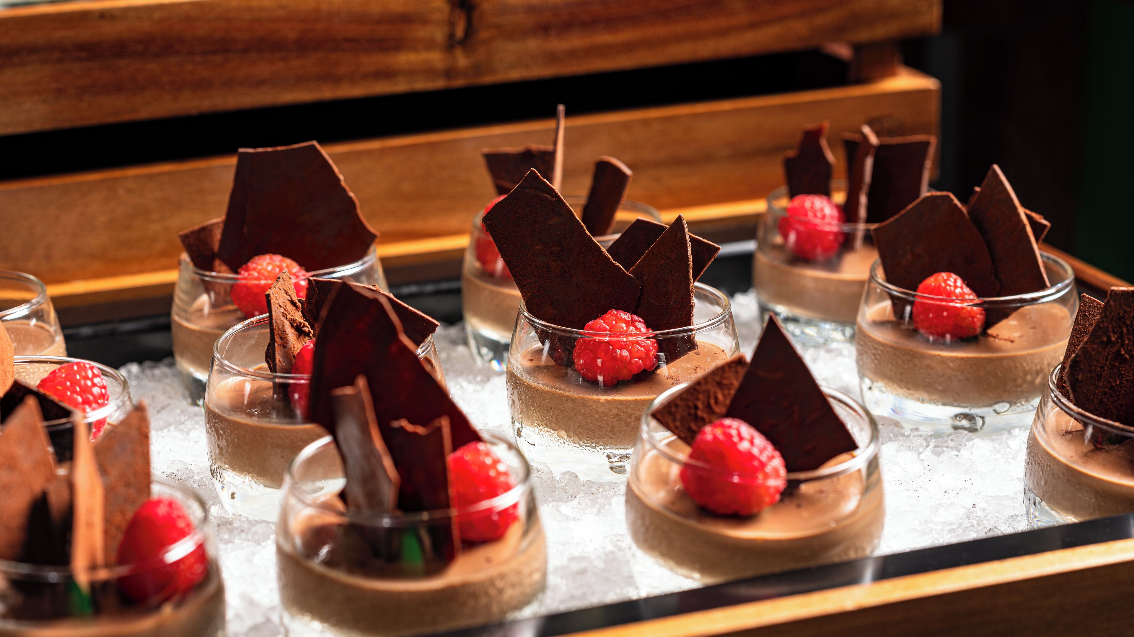 A dessert display with chocolate mousse cups topped with chocolate shards and raspberries.