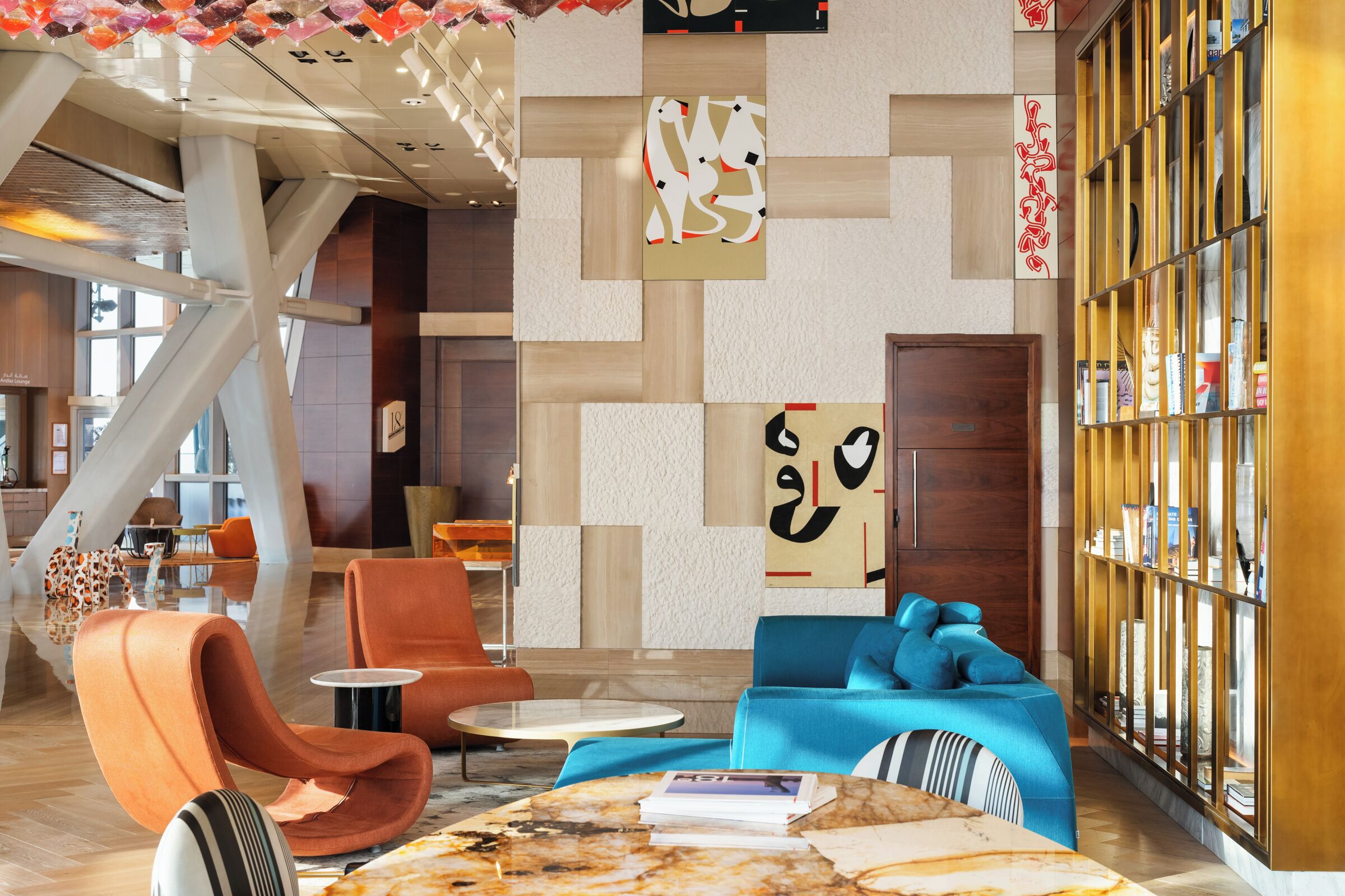 A modern lobby with a geometric wall design, seating areas, and a bookshelf.