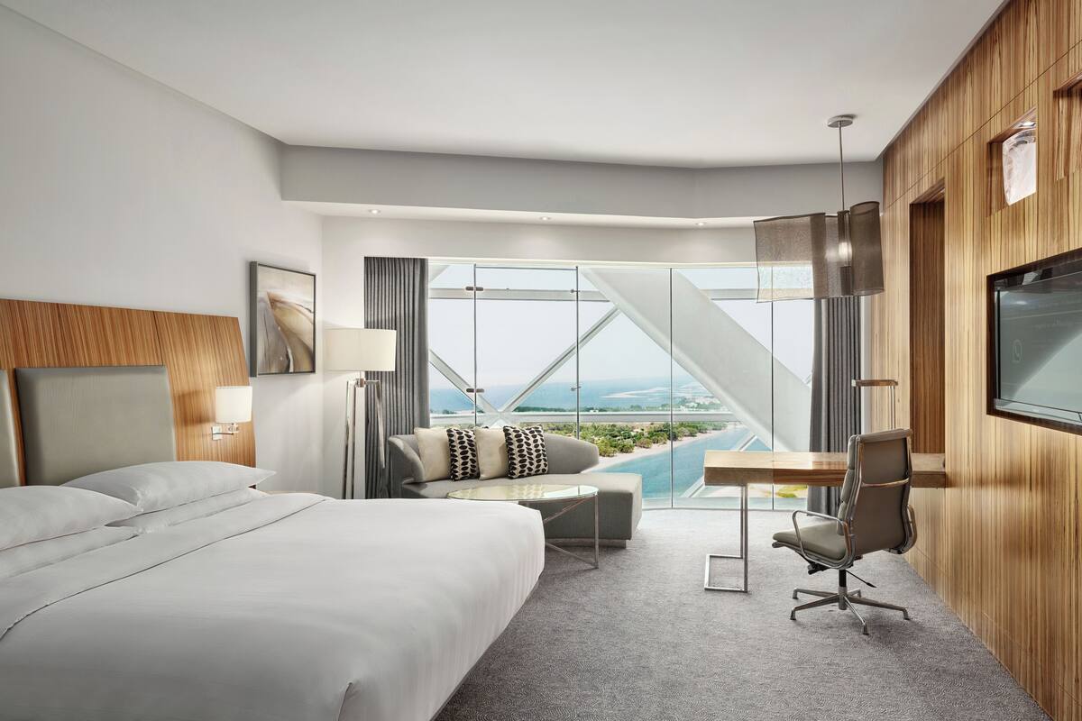 Ein modernes Hotelzimmer mit einem großen Bett, einem Schreibtisch mit Stuhl, einem Fernseher und Meerblick.