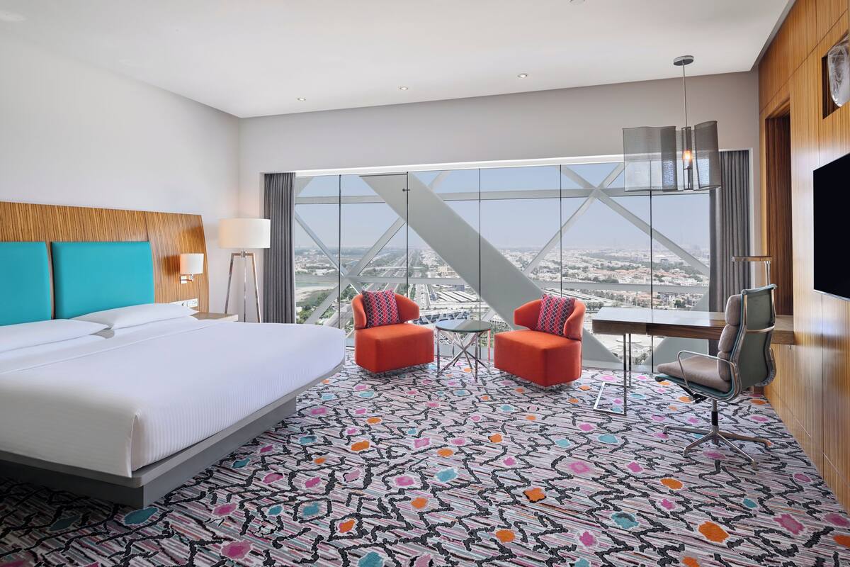 Ein Hotelzimmer mit einem großen Bett, zwei Sesseln, einem kleinen Tisch und einem Fernseher.