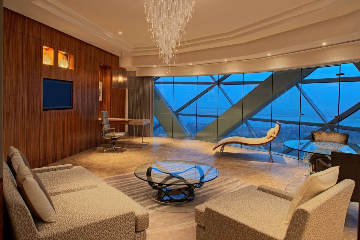 Ein modernes Interieur mit Glastisch, gepolsterten Sitzgelegenheiten, einem Wand-Fernseher und Blick durch große Fenster.