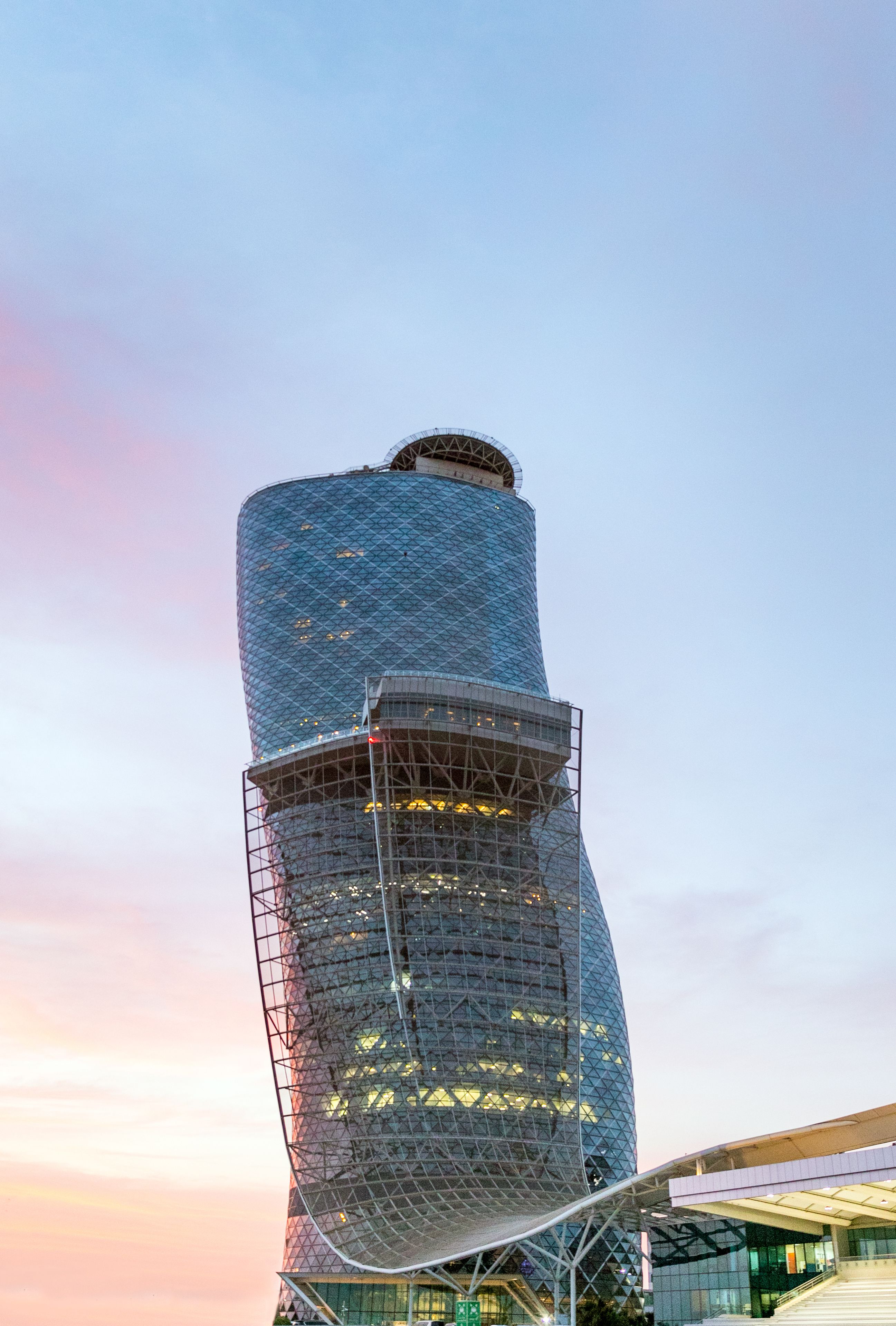 Um edifício moderno, cilíndrico e com um design singular em espiral, apresentando fachada de vidro e andaimes de metal.