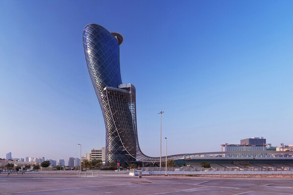 A modern, curved skyscraper with a reflective glass facade, surrounded by a spacious urban area with a clear sky. - ANDAZ CAPITAL GATE ABU DHABI, BY HYATT (Abu Dhabi)