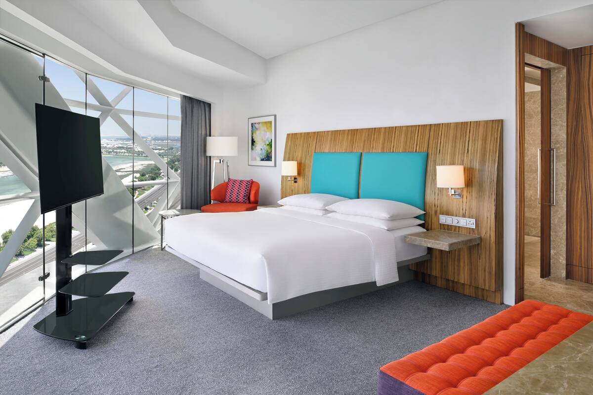 Ein modernes Hotelzimmer mit einem großen Bett, einem Fernseher und Blick auf die Stadt.