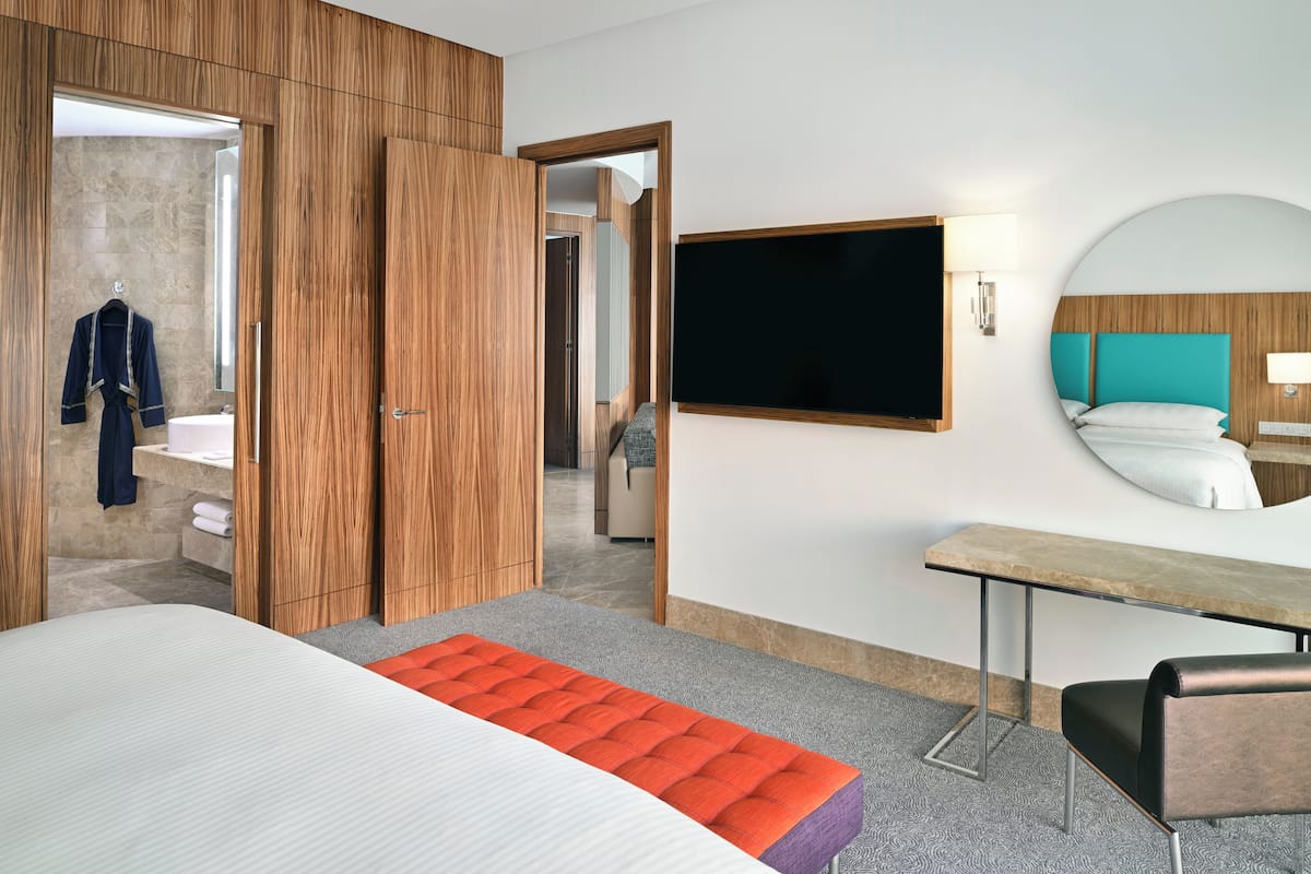Ein modernes Hotelzimmer mit einem großen Bett, einem Holzschrank, einem Schreibtisch und einem Fernseher.