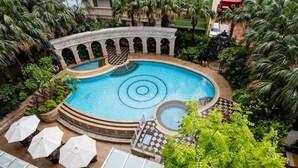Ein runder Pool mit einer zentralen Fontäne, umgeben von Palmen und einem Steinkunstwerk.