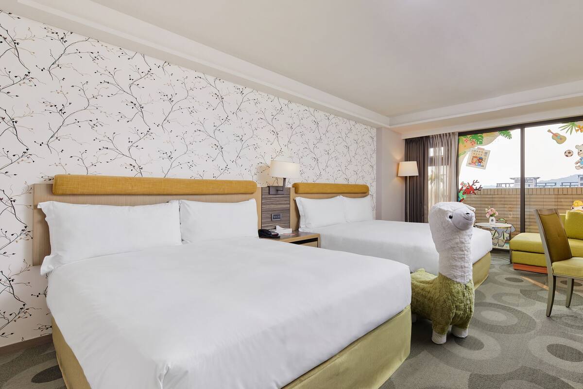 Hotelkamer met twee bedden, een bureau, een stoel, een televisie en een raam met gordijnen.