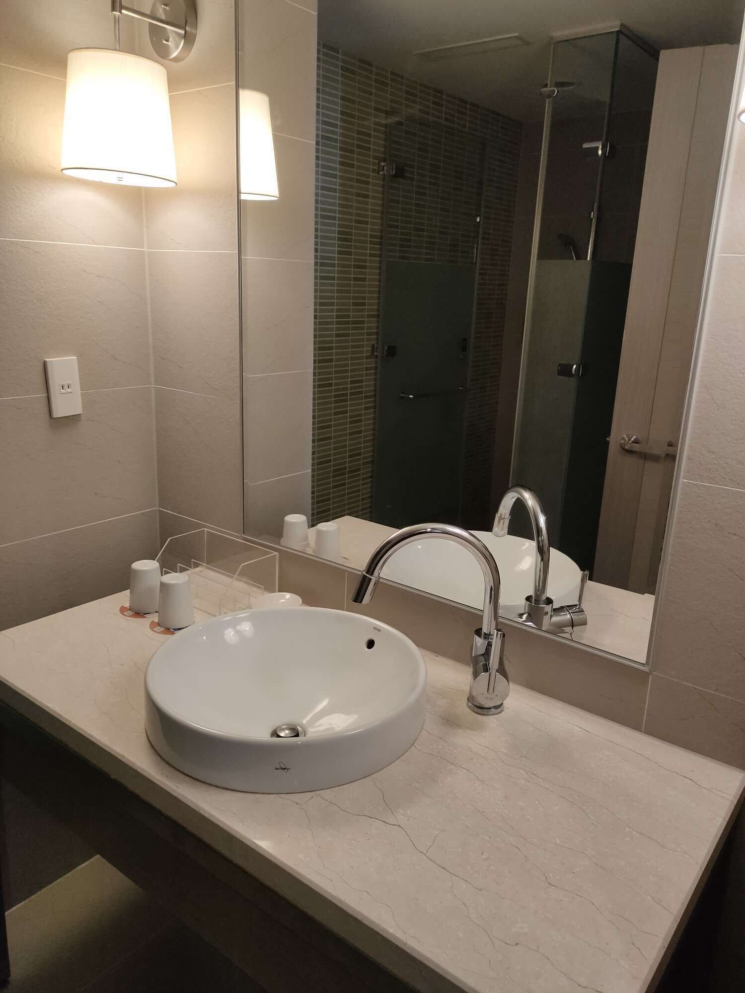 A bathroom with a round sink, a mirror, and a shower area.