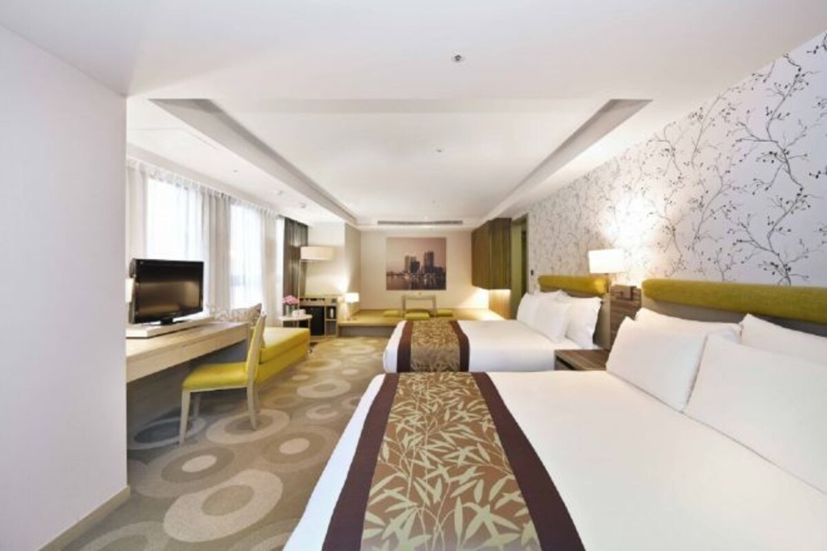 Une chambre d’hôtel avec deux lits, un bureau avec une télévision, une chaise et une fenêtre avec des rideaux.