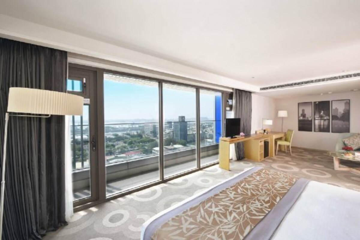 Una habitación de hotel con un ventanal grande, una cama, un escritorio y una silla.
