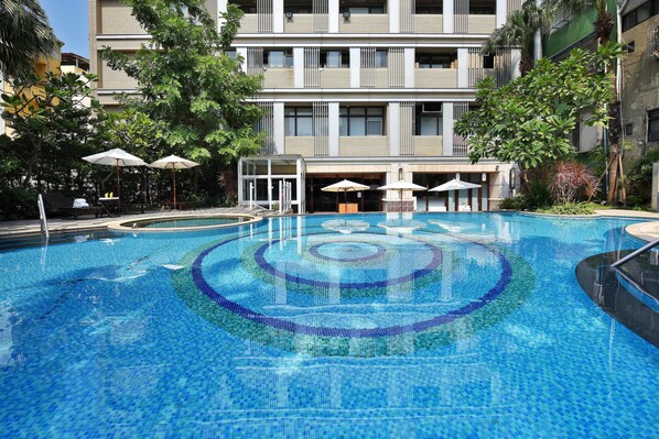 A swimming pool with a geometric tile design, surrounded by lounge chairs and umbrellas, with a multi-story building in the background. - Fullon Hotel Kaohsiung (Kaohsiung)